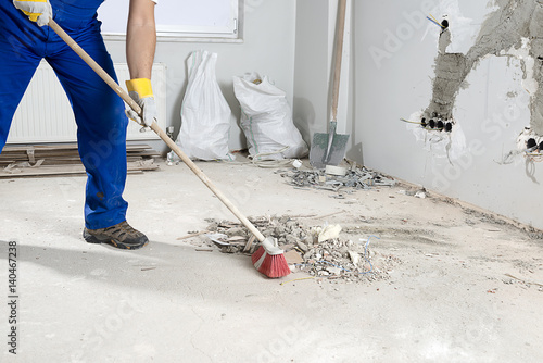 Manual worker sweeping rough rubble at construction site using broom. 