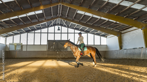 Junge Reiterin trabt mit Hannoveraner Pferd in der Reithalle