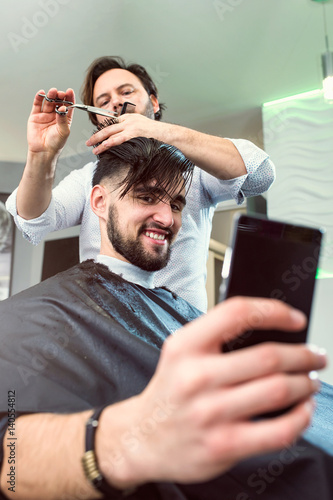 Men in a Barber Shop Using Smart Phone While Having Haircut