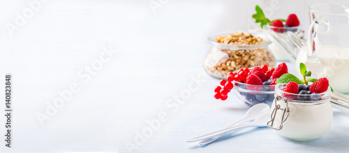 Yoghurt with muesli, raspberry, blueberry and mint in glassware on a blue background