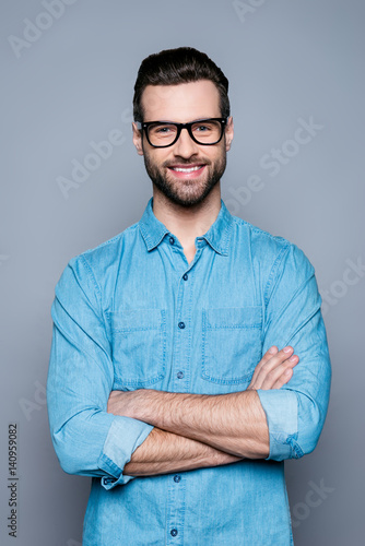 Portrait of happy fashionable handsome man in jeans shirt and glasses crossing hands and smiling