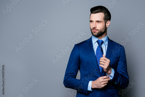 Portrait of serious fashionable handsome man in blue suit and tie buttoning cufflinks