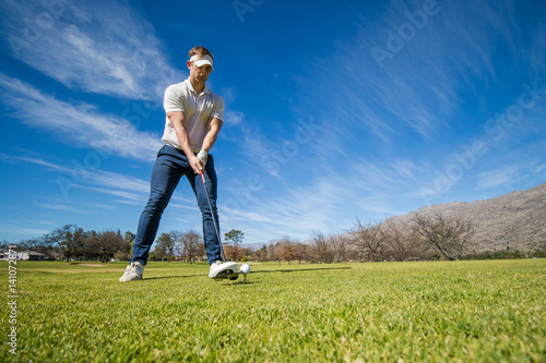 Wide angle view of a golfer teeing off from a golf tee on a bright sunny day on a golf course in south africa.