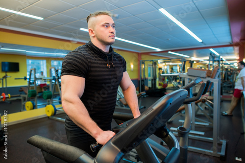 Attractive young muscular man while running on a treadmill in gym