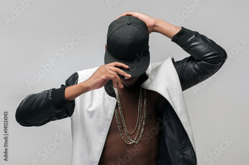 Black afroamerican rebellious rapper on grey background. Closed face, rejection, separated, reluctance to see, breaking off. Ghetto, challenge to society, cheeky, cool