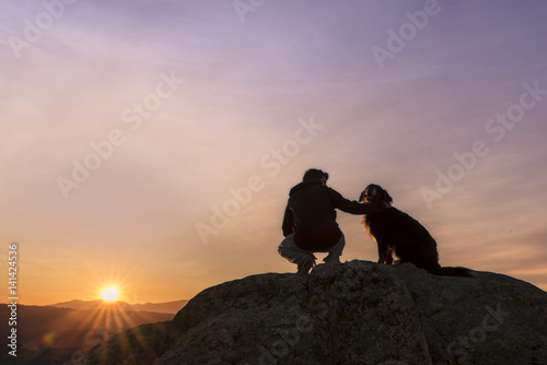 Man and his faithful companion watching the sunrise on top of the mountain