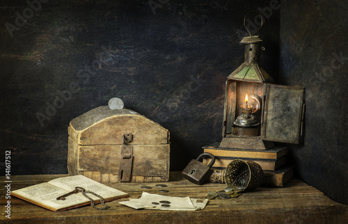 Classic still life with old savings box placed with vintage lamp,old books.coins, key and lock on rustic wooden background..