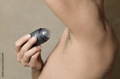 young man applying deodorant to his armpits