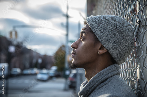 A young, hip man poses for a pensive portrait along a fence in NYC