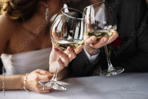 Wedding couple with glasses of wine in hands mark the wedding ceremony in the restaurant at the table. bride and groom with earrings in a dark suit blurred focus only hands and glasses of wine