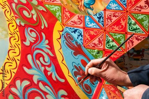 Hand of a sicilian cart painter while finishing some colored details. Workshop of the sicilian folkloric craftsmanship Rosso Cinabro, Ragusa Ibla