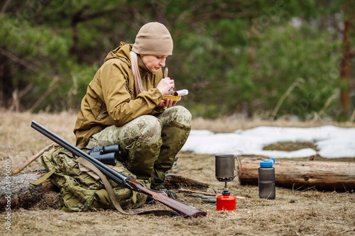 Female hunter preparing food with a portable gas burner in a winter forest.