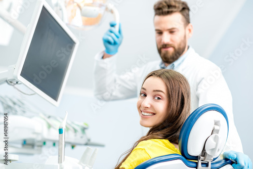 Portrait of a woman with toothy smile sitting at the dental chair with doctor on the background at the dental office