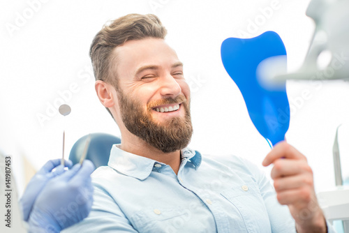 Handsome male patient looking at his beautiful smile sitting at the dental office