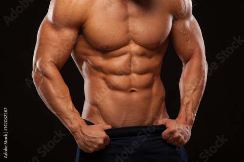 Strong Athletic Man - Fitness Model showing Torso with six pack abs. stands straight and puts his hands in trousers. isolated on black background with copyspace