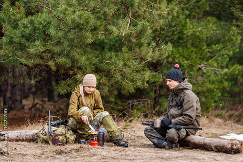 .Two hunters are eating together in the forest. Bushcraft, hunting and people concept