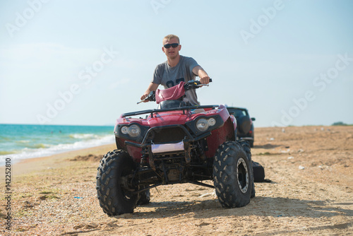 A young guy in sunglasses is riding an ATV on the beach