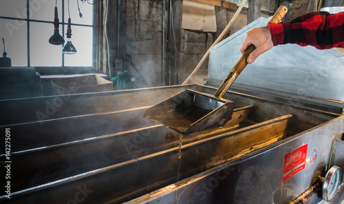 steam rising off of boiler evaporating maple tree sap to make maple syrup in sugar house, dripping syrup from ladle to test how thick syrup has become ; an early spring tradition in Vermont 