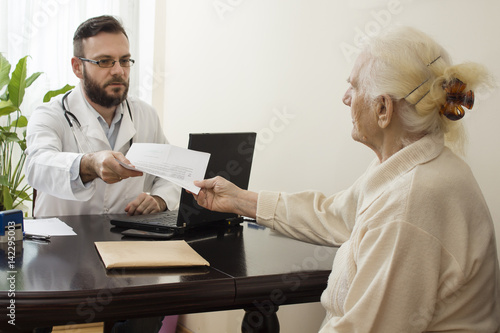 Lekarz podaje zastrzyk w brzuch starej kobiecie. Lekarz geriatra przyjmuje pacjenta w gabinecie. Stara kobieta u lekarza geriatry.Lekarz geriatra przyjmuje pacjenta. Odbiera dokumenty od pacjentki.