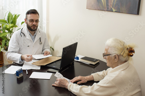 Lekarz podaje zastrzyk w brzuch starej kobiecie. Lekarz geriatra przyjmuje pacjenta w gabinecie. Stara kobieta u lekarza geriatry.Lekarz geriatra przyjmuje pacjenta. Odbiera dokumenty od pacjentki.