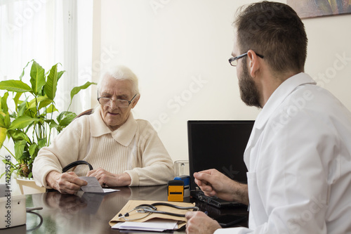Gabinet lekarski. Lekarz przyjmuje pacjenta. Pacjentka, stara kobieta czyta zapis na recepcie wystawionej przez lekarza.