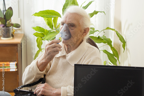 Stara kobieta podczas inhalacji. Pacjentka trzyma maseczkę inhalatora. Atak astmy. Inhalacja górnych dróg oddechowych. 