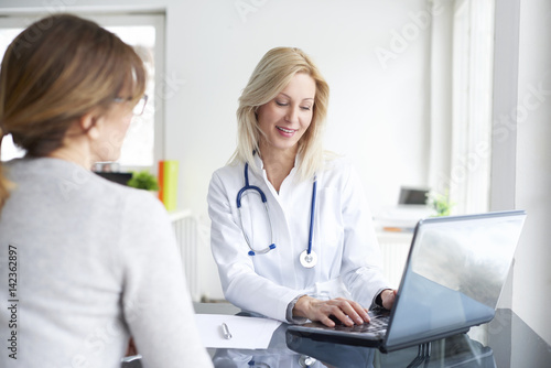 Doctor and her patient. Shot of a middle aged female doctor sitting in front of laptop and consulting with her patient.