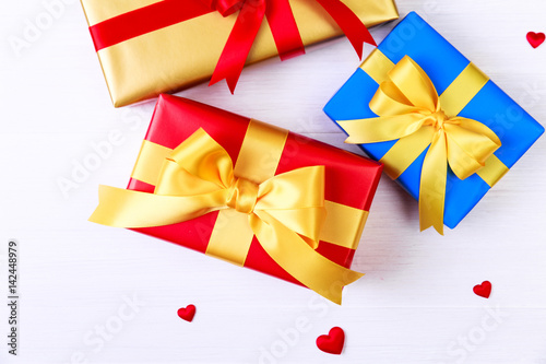 Gift boxes with red satin hearts. Presents wrapped with yellow ribbon. Christmas or birthday packages. On white wooden table.