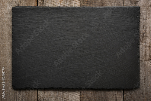 Black slate tile on wooden background. Top view.