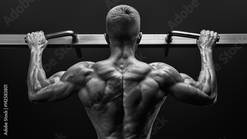 Power muscular bodybuilder guy doing pullups in gym. Fitness man pumping up lats muscles. Fitness and bodybuilding training health lifestyle concept