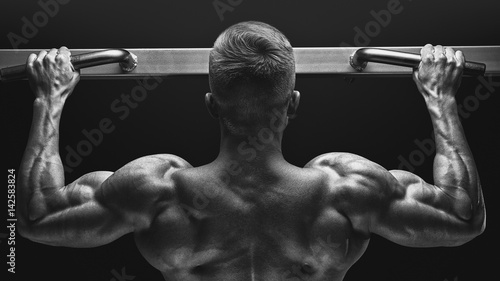 Close-up photo of attractive muscular bodybuilder guy doing pullups in gym. Fitness man pumping up lats muscles. Bodybuilding and fitness training health lifestyle concept