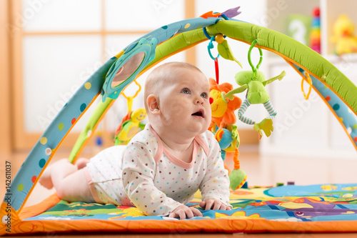 Happy seven months baby girl plays lying on colorful playmat