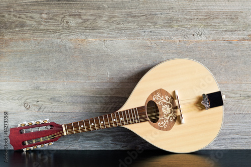 Front view of a reclined wooden flatback mandolin on a black table with a weathered wood background