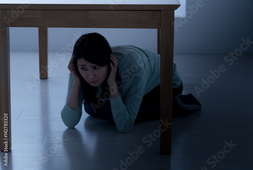 テーブルの下に隠れる女性、地震、震災、災害