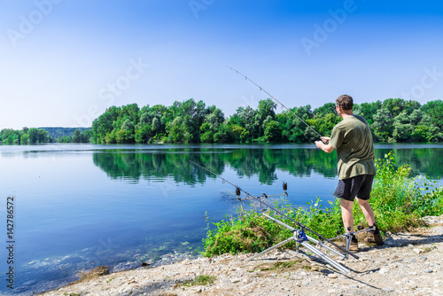 Fishing adventures, carp fishing. Angler is fishing with carpfishing technique in a beautiful summer day with light blue sky