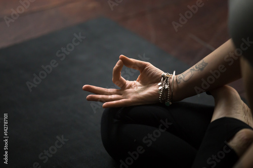 Close up of young woman hand with tattoo and wrist bracelets practicing yoga, sitting in Padmasana exercise on black mat, Lotus pose with mudra gesture, working out, meditating, copy space background