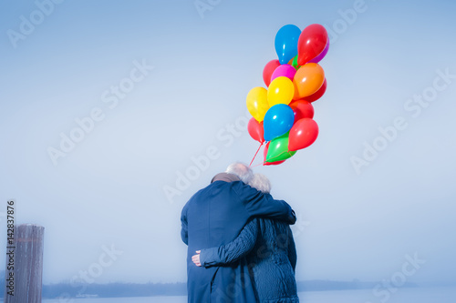 Seniorenpaar eng umschlungen am See mit Luftballons