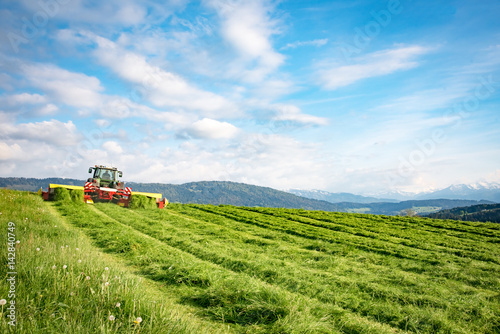 Mähen einer Wiese für Silage mit Alpen im Hintergrund