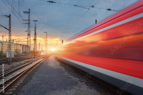 High speed red passenger train on railroad track in motion at sunset. Blurred commuter train on the railway station and sunlight. Railroad travel, railway tourism. Industrial landscape in Germany