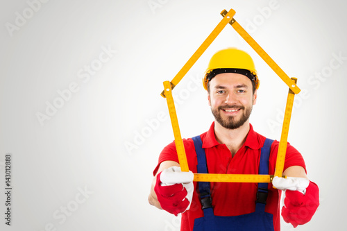 home improvement - handyman with house shaped ruler in hands on gray background with copy space