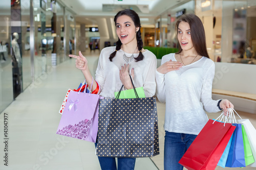 Two cute girl walks in mall with gift bags.