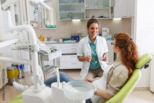 A professional female dentist, equipped with a bright smile, converses with her red hair female patient, carefully explaining the upcoming treatment, and ensuring her comfort throughout the process.