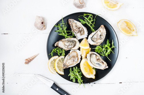 Oysters with lemon fruit on a black plate on a white wood table