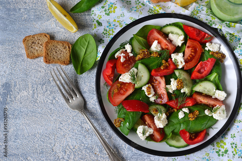 Vitamin salad with tomatoes, spinach and feta cheese on betonnoom background. Top view.