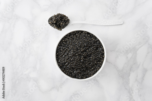 black caviar in bowl and on white shoop on marble background