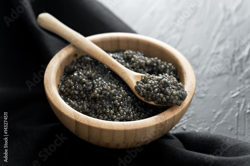 black caviar in wooden bowl on black background