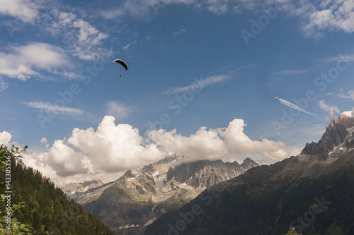 Paraglider flies over the tops of the mountains in summer sunny day