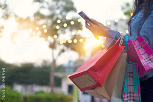 Kobieta używa smartphone z torba na zakupy w rękach