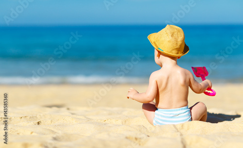 baby boy sit back with toys on beach