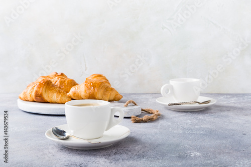 White cups of coffee and croissants on light gray background, selective focus. Healthy breakfast concept with copy space.